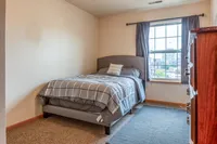 Cozy bedroom with plush bed, large window offering city views, and elegant wooden dresser.