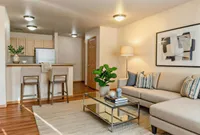 Inviting living space with chic modern decor, featuring a cozy beige sectional, glass coffee table, and a stylish breakfast bar with seating.