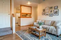 Charming open-concept living room with cozy sofa, elegant rug, stylish coffee table, and modern kitchen backdrop.