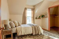 Cozy bedroom retreat featuring elegant beige decor, large window for natural light, and stylishly adorned shelves with plants and art.