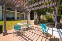Charming outdoor patio with pergola, colorful seating, and barbecue area amidst lush greenery.