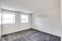 A bright, empty bedroom in Bright Meadows Townhomes featuring two windows and soft carpeting.