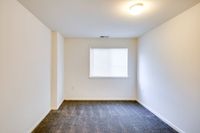 Spacious empty room in Allyson Garden Apartments II, showcasing a cozy carpet and a modern light fixture.