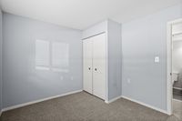 Bright and inviting bedroom with soft gray walls, plush carpet, and a spacious closet, perfect for cozy living.
