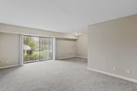 Bright and spacious living room with lush garden views through large sliding glass doors, featuring plush carpet and neutral walls.