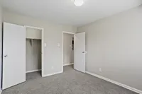 Bright and spacious bedroom with fresh grey carpeting, featuring a large closet and sleek white doors, perfect for modern living.