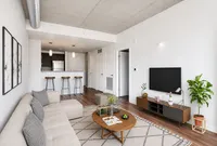 Modern apartment living room with sleek decor, cozy sofa, hardwood floors, and an open kitchen with bar seating.