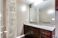 Elegant bathroom featuring a large mirror, sleek granite countertop, and modern dark wood cabinetry.