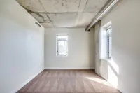 Bright and airy room with modern concrete ceiling, large windows, and plush carpeting, perfect for a cozy retreat.