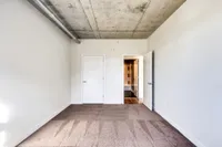 Modern room with an industrial concrete ceiling, accented by clean white walls and inviting carpet flooring, leading to a bright hallway.