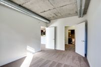 Contemporary apartment featuring a spacious room with stylish exposed ductwork, plush carpeting, and ample natural light, leading to a modern kitchen and bathroom.