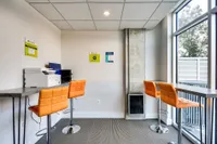 Modern apartment business center with vibrant orange bar stools, sleek workstations, and large windows for natural light.