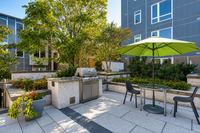 Modern outdoor patio with stylish barbecue grill, lush greenery, and a charming seating area under a vibrant green umbrella.