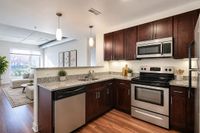 Modern kitchen with stainless steel appliances and granite countertops opening to a bright living room with large window views.