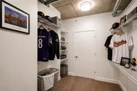 Modern closet with sports-themed decor featuring jerseys, caps, and framed cityscape artwork, creating a personalized and inviting storage space.