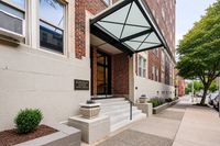 Inviting entrance to Jefferson House Apartments with elegant modern canopy, lush greenery, and charming brick facade, offering a glimpse of urban living at its finest.