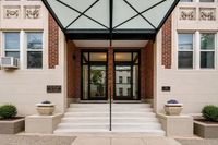 Elegant entrance of Jefferson House Apartments, featuring modern glass doors, red brick facade, and stylish planters.