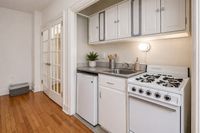 Charming and compact kitchen with elegant white cabinetry, a cozy stove, and warm hardwood floors, ideal for efficient living.