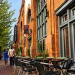 Charming street view of a vibrant urban setting with outdoor dining in front of a historic red brick building.