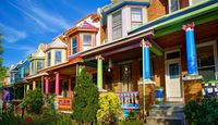 Vibrant historic row houses with colorful facades and charming architectural details, framed by lush greenery under a bright blue sky.