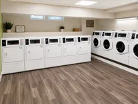 Modern apartment laundry room featuring multiple high-efficiency washers and dryers with sleek hardwood flooring and ambient lighting.