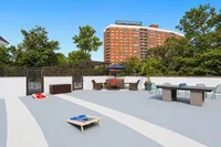 Vibrant apartment community terrace with stylish seating, games, and lush greenery under a clear blue sky.