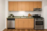 Contemporary kitchen with sleek stainless steel appliances, natural wood cabinets, and a chic green countertop, offering a modern cooking space.