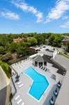 Inviting aerial view of a modern apartment complex featuring a pristine swimming pool, lounge chairs, and vibrant green surroundings.