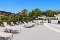 Luxurious rooftop terrace with relaxing lounge chairs and elegant pergolas, surrounded by lush greenery and a bright blue sky.