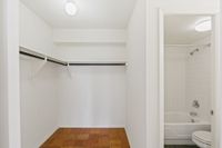 Spacious walk-in closet with hardwood flooring and adjacent bathroom featuring a sleek white bathtub and modern fixtures.