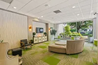 Contemporary lobby with stylish seating, vibrant green accents, and floor-to-ceiling windows showcasing lush outdoor views.