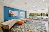 Inviting lounge area with modern curved sofa, vibrant artwork, and floor-to-ceiling windows overlooking a poolside view, creating a stylish and relaxing atmosphere.