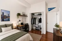 Chic bedroom with a cozy bed, modern workspace, and organized closet on elegant wooden floors.
