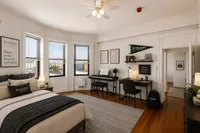 Charming bedroom with hardwood floors, abundant natural light from large windows, and a cozy study area, perfect for relaxation and productivity.