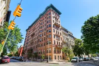 Charming corner building with classic architecture, nestled in a vibrant neighborhood with lush green trees and bright urban surroundings.