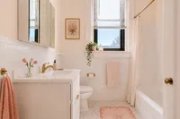 Elegant bathroom showcasing a pristine white vanity with gold fixtures, soft pink accents, and a serene atmosphere.