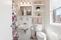 Charming bathroom featuring elegant lighting, floral shower curtain, and crisp white tiles with modern shelving.
