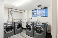 Modern apartment laundry room with four sleek washers, bright lighting, and informative posters on the wall.