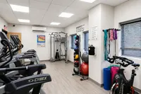 Chic apartment gym with modern equipment, including treadmills, weight rack, and exercise mats, flooded with natural light.