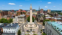 Breathtaking aerial view of historic city square featuring a majestic monument, surrounded by charming architecture and lush greenery.