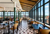 Vibrant restaurant with large panoramic windows offering stunning city views, featuring stylish decor and modern dining ambiance.