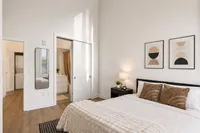 Bright and inviting bedroom with modern decor, featuring a cozy bed, chic wall art, and an en suite bathroom. Natural light enhances the serene aesthetic.