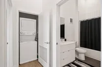 Modern apartment bathroom with sleek vanity, bright lighting, and in-unit stacked washer and dryer for convenience.