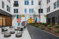 Vibrant urban courtyard featuring modern seating, artistic wall mural, and lush greenery in a stylish apartment complex.