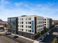 Contemporary apartment complex with modern architecture, showcasing ample parking and vibrant urban surroundings.