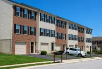 Charming row of modern townhouses with brick exteriors, sleek garages, and manicured lawns under a clear blue sky.