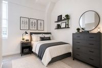Elegant bedroom with modern decor, featuring a cozy bed, stylish artwork, and a sleek dresser with a round mirror.