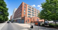Charming urban apartment building with a classic red brick exterior, nestled in a lively city street lined with lush green trees.