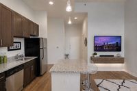 Contemporary kitchen and living area featuring sleek brown cabinets, stainless steel appliances, stylish island counter, and wall-mounted TV with city skyline view.
