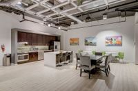 Contemporary kitchen and dining area featuring sleek cabinetry, modern appliances, elegant island with bar seating, and stylish artwork under industrial-style ceilings.